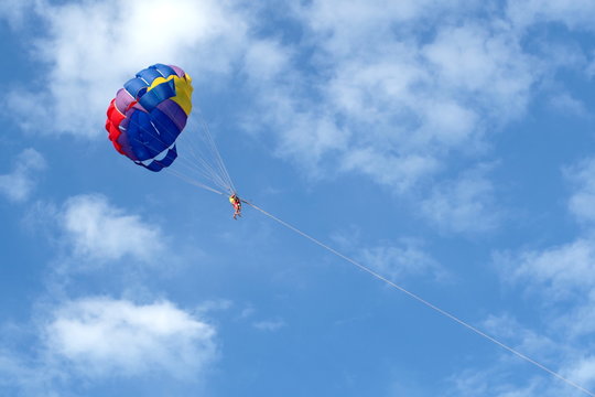 Bright colorful parachute in the air, blue sky and white clounds.
