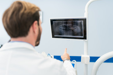 Happy smiling dentist looking at the screen, an teeth x-ray in a modern dental clinic.