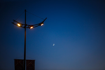 Street lamp at night against the dark blue sky and the moon. Futuristic street lighting in the form of a space lantern