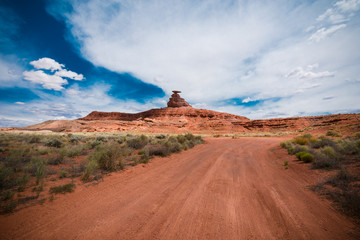 Dirt road trail leads to the Mexican Hat rock formation in the Utah desert. Wide angle