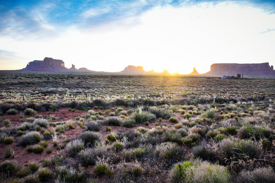 Bright sunrise in Monument Valley Utah, with lots of desert sagebrush in the foreground. Sun peaking over the rock formations