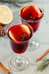 Two glassses with winter Christmas traditional mulled wine with orange slices, anise and cinnamon sticks among winter decorations.