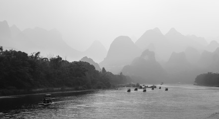 Tourist boats with tourists traveling the magnificent scenic route along the Li river from Guilin to Yangshuo in the haze, Xingping, China. Black and white photography