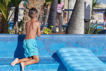 Cute Caucasian boy playing with inflatable mattress in pool at resort on family vacation.