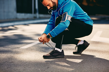 Male runner crouching and tying shoelace. Sportswear on, earphones in ears. Healthy lifestyle concept.
