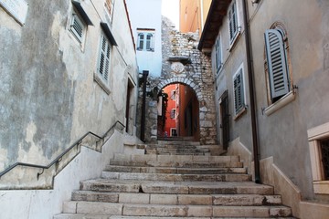 Fototapeta na wymiar Croatia, Rovinj, August 2018: Adriatic, streets of a small seaside town, sunny hot summer day, old weathered houses, windows with multi-colored shutters, drying clothes on ropes, yachts, blue sea.