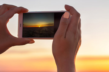 Girl makes a photo of sunset by phone