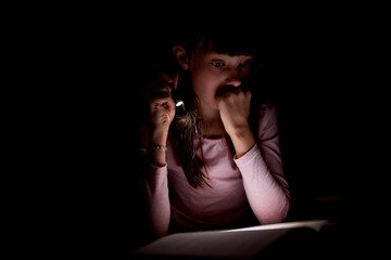 little girl is reading a book with a flashlight in a dark room at night