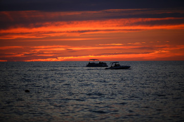 Orange sunset sky over the sea with boats. The blue outlines of the mountains on the horizon is the coastline of Batumi