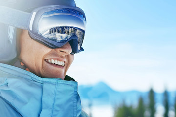 Close up of the ski goggles of a man with the reflection of snowed mountains.  A mountain range reflected in the ski mask.  Portrait of man at the ski resort on the background of mountains and sky - obrazy, fototapety, plakaty