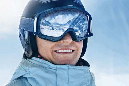 Close up of the ski goggles of a man with the reflection of snowed mountains.  A mountain range reflected in the ski mask.  Portrait of man at the ski resort on the background of mountains and sky