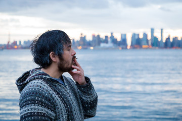 Fototapeta premium A young man smoking a joint with downtown Vancouver, BC, in the background shortly after Canadian marijuana legalization.