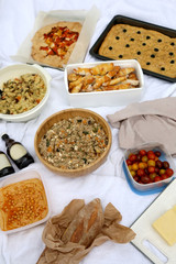 Picnic blanket with various food: bread, buckwheat and vegetable salad, hummus, cheese, cherry tomatoes, pastry, focaccia and galette. Selective focus. 