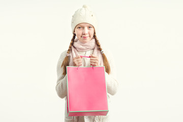 Girl in a winter hat and a warm sweater with a pink bag in her hands. Christmas gifts and purchases.
