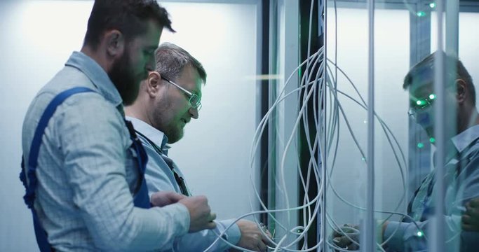 Medium shot of two people working in a data center with cable to repair rows of server racks and discuss their work