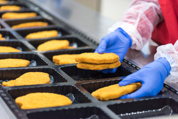 The worker in the factory places the chicken schnitzel