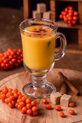 Hot beverage of sea-buckthorn berries in glass cup. Rustic style.