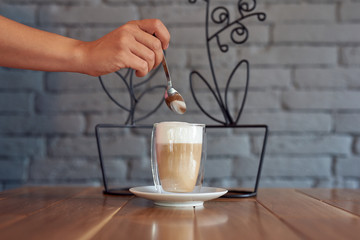 Transparent glass mug with latte or cappuccino and female hand with a teaspoon