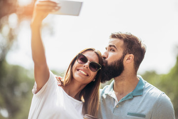 Young couple using mobile phone taking a selfie in the park