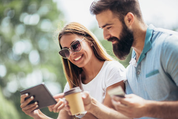 Cheerful young couple sitting on a park bench and uses a digital tablet for online shopping