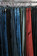 Denim pants in different colors on hangers in a clothing store. The concept of shopping and sales. Background for design on the theme of fashion or second hand.