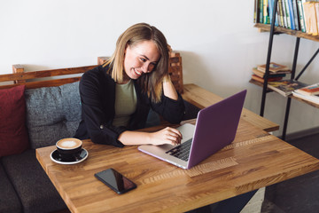 young girl communicates on a laptop with people and laughs in a cafe