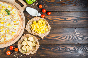 Obraz na płótnie Canvas Food design. Big pizza with chicken and pineapples on a round cutting board on a dark wooden background. Ingredients.