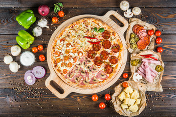 Large author's meat pizza from four different parts on a round cutting board on a dark wooden background. Ingredients.