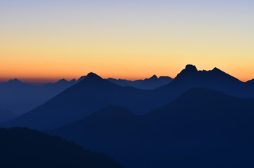 Fototapeta na wymiar Beautiful morning mood in the Allgaeu Alps at the border region of Germany and Austria. Blue silhouettes of multiple mountains and mountain ranges at sunrise with orange sky. Copy space.