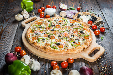 Big pizza with cheese, tomatoes, black olives and paprika on a round cutting board on a dark wooden background. Ingredients.