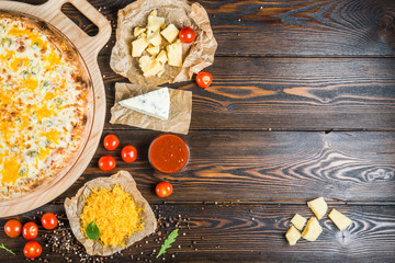 Obraz na płótnie Canvas Food background design. Pizza with three kinds of cheese on a round cutting board on a dark wood. Ingredients.