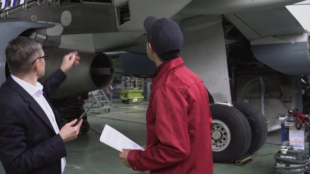 Aircraft repair in the hangar. Two engineers discuss how to repair the aircraft. Plant for the production of aircraft. Aviation. 4k