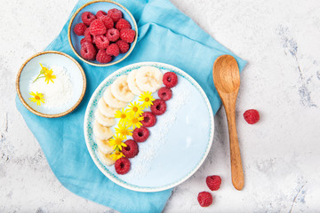 Blue yogurt smoothie bowl made with blue spirulina powder, fresh berries, banana and yellow flowers, top view