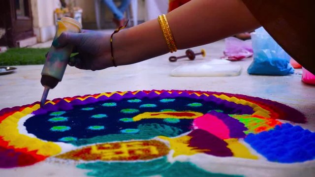 Girl hands using funnel cone to create rangoli using colored powders on the hindu festival of diwali or deepavali. This traditional decoration is handmade with colorful powders and consists of