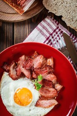 Slices of smoked bacon and fried egg on a red plate