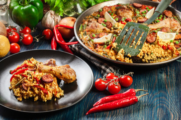 Traditional paella with chicken legs, sausage chorizo and vegetables served on black plate