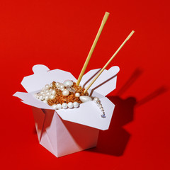 Wok box filled with jewelry and bijoux on a red background. Creative concept.