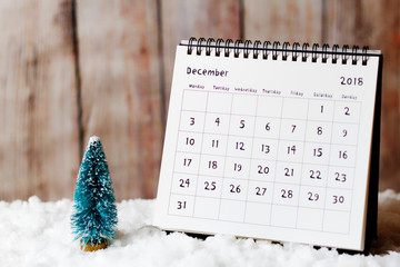 December 2018 calendar on the snow and little Christmas tree decoration. Wooden wall in the...