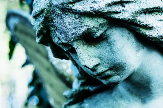 Sad winged angel at an old cemetery. Vintage styled image of ancient statue. Fragment of sculpture. (religion, faith, death, resurrection, eternity concept)