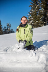 Young beautiful woman playing in snow in green jacket