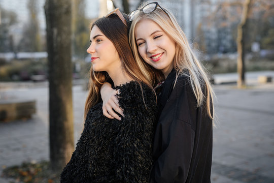 Two pretty girls hug each other on the city street and smile