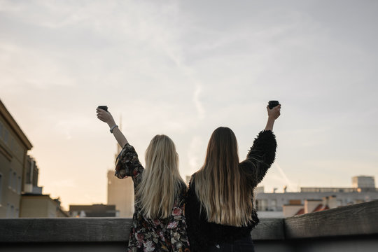 Two gitls stand on the rooftop and have a drink