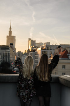 Two gitls stand on the rooftop and have a drink