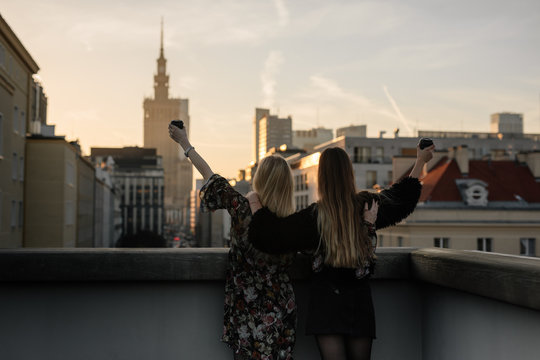 Two gitls stand on the rooftop and have a drink