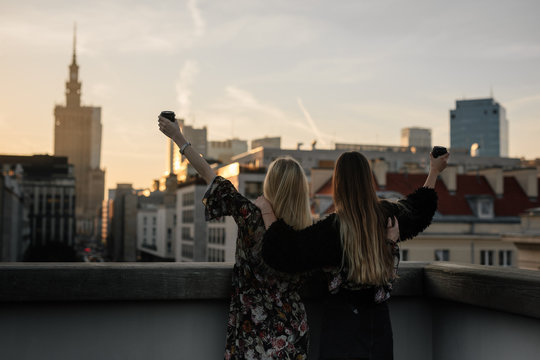 Two gitls stand on the rooftop and have a drink