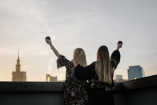 Two gitls stand on the rooftop and have a drink
