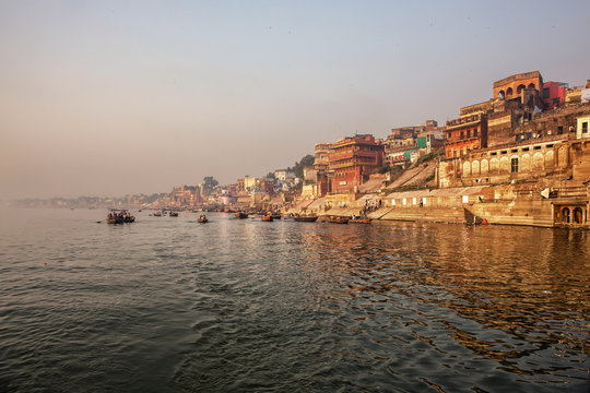 aranasi Ganges river ghat with ancient architectural buildings and temples as viewed from a boat on the river at sunset