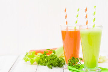 Carrot and celery juice with fresh vegetables on bark plates on wooden background.