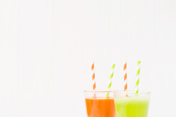 Carrot and celery juice in glasses with straws isolated on wooden background with copy space.