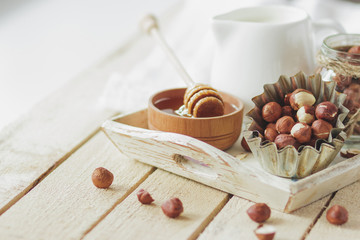 Honey in the wooden bowl, hazelnuts and jar with milk on the wooden tray